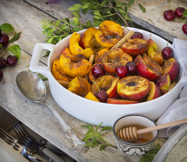 Hot cinnamon peaches in a white dish on a wooded table. 