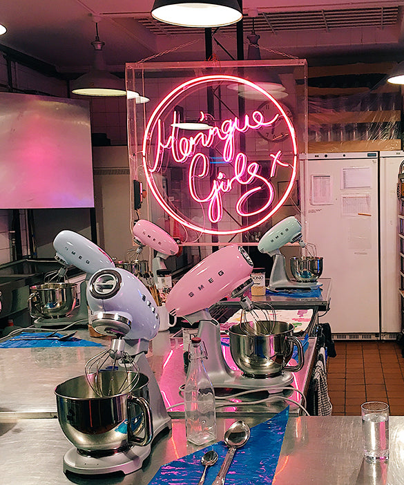 Table full of mixers in pink, purple and green colors with "Meringue Girls" in pink text lighting. 