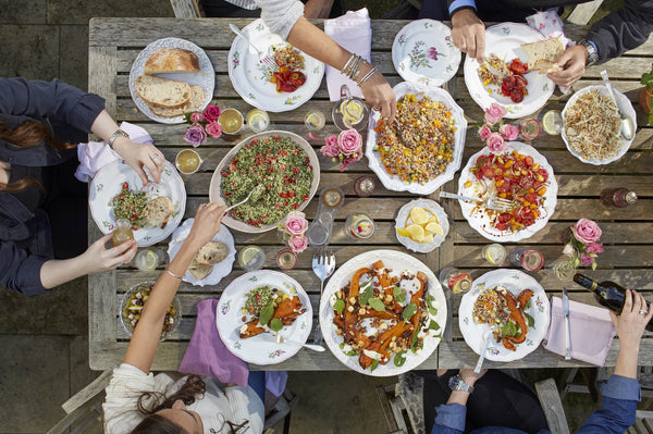 Top view of variety of foods on plates with people sitting at table. 