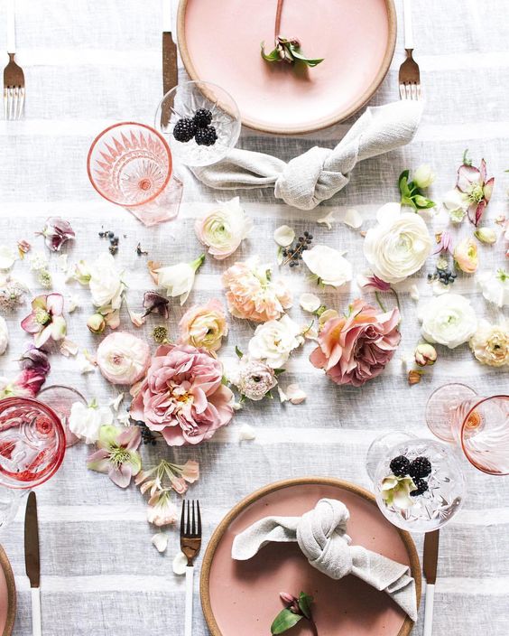 Top view of pink table setting surrounded by flowers on white tablecloth.