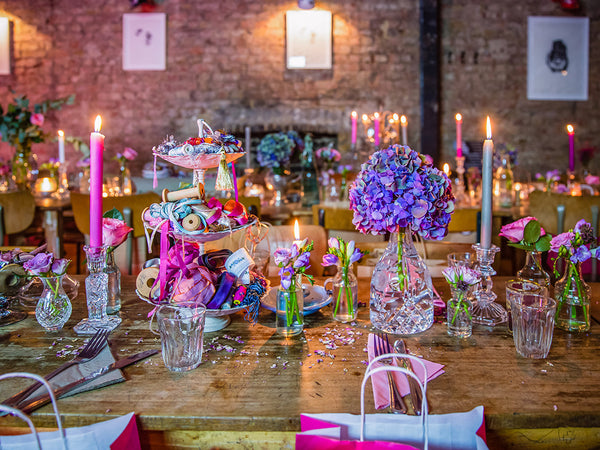 Table setting with colors of pink and purple. Surrounded by flowers, candles, and clear table settings.