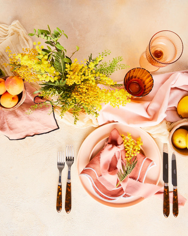 Top view of table setting and stemware with light pink napkins surrounded by lemons and flowers. 