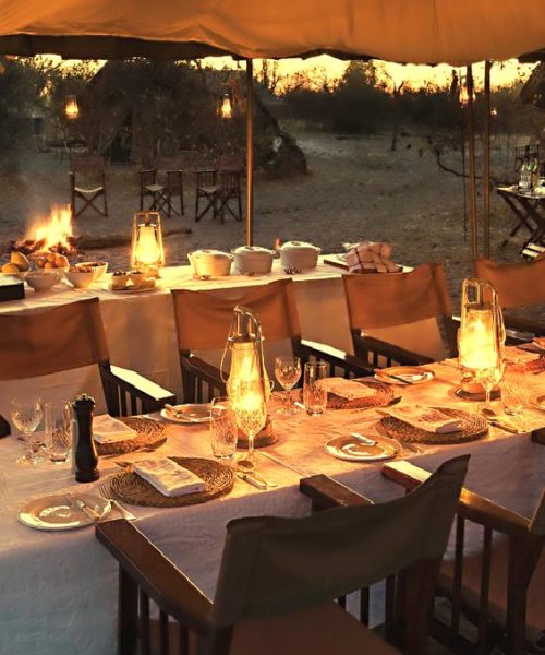 Outdoor evening table setting with white tablecloth, wood chair and candles. 