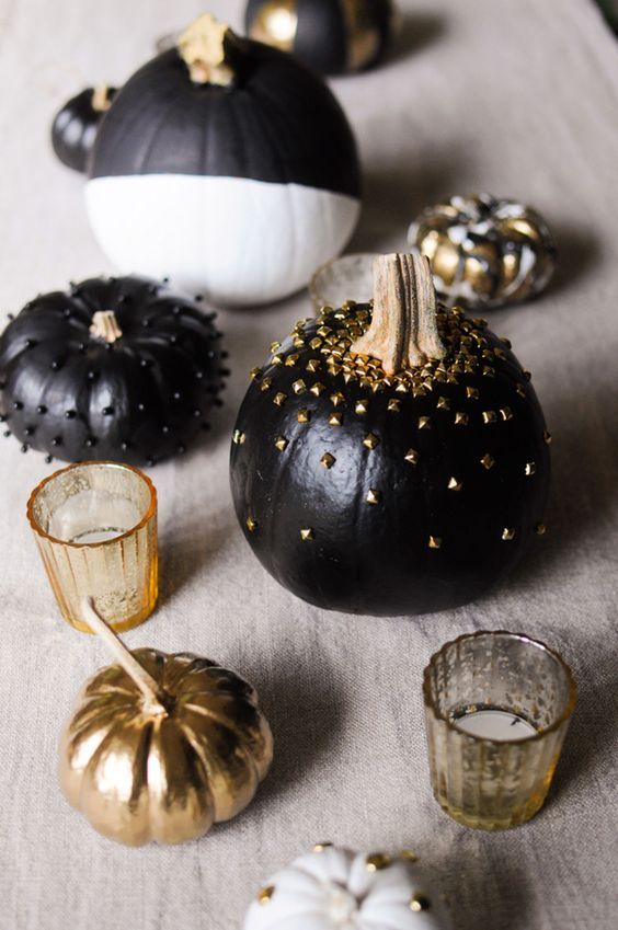 Gold and black painted pumpkins surrounded by small gold candles. 