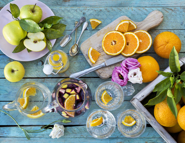 Top view of sliced oranges and apples with clear cups and silverware on a blue table. 
