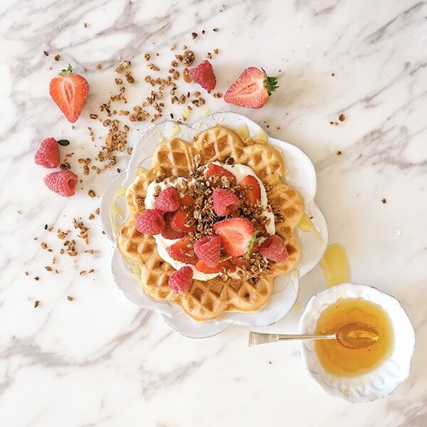 Top view of waffles topped with cream and strawberries on white dish with white marbled table background.
