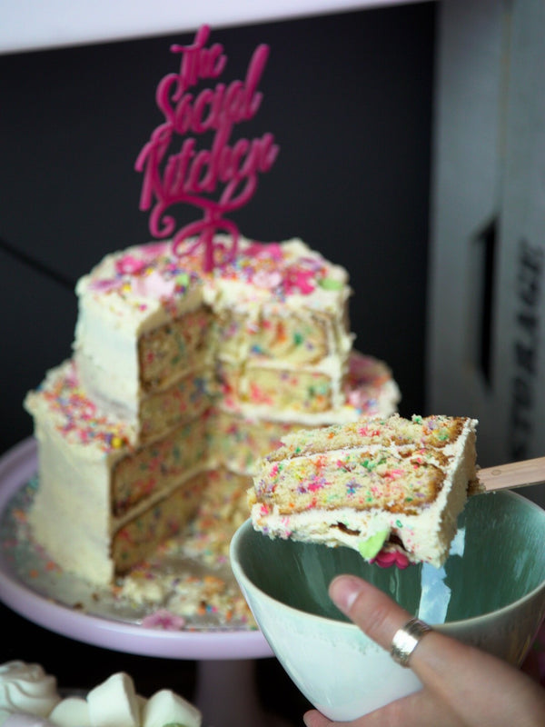 The Social Kitchen cake topper on cake with slices being served. 