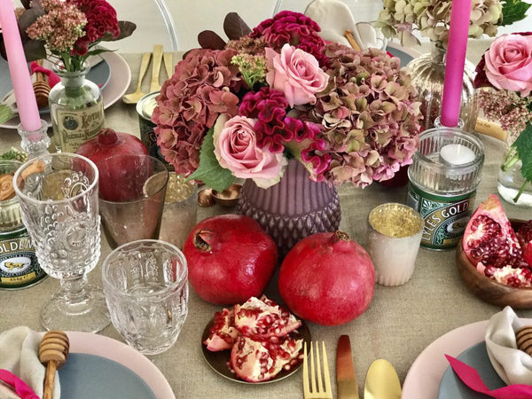 Top view of flowers in a vase surrounded by pomegranates, candles, dinnerware and drinking glasses.  