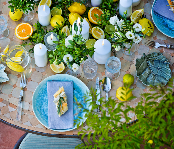 Top view of table setting surrounded by greenery and citrus fruits on a round wooded table. 