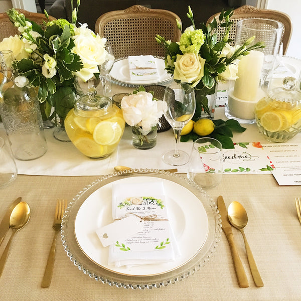 Top view of plate setting on beige and white tablecloth with candles, flowers and lemonade.