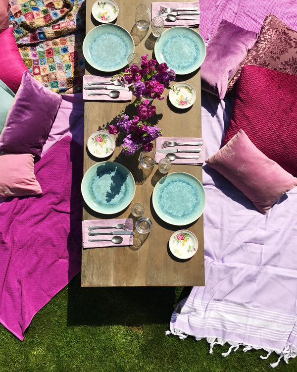 Top view of outdoor picnic table settings with mixed pink pillows and blankets. 