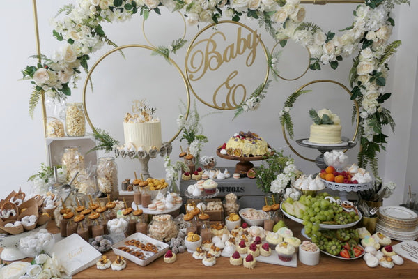Table full of hors d'oeuvres and cakes with text: Baby E. 