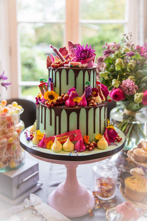 Two tiered green frosted cake with chocolate drizzle, flowers and candies. 