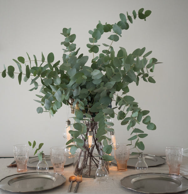 Vase full of eucalyptus surrounded by silver table settings. 