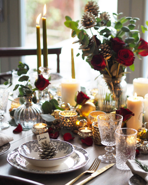 Table setting on wood table surrounded by candles, drinking glasses and flowers. 