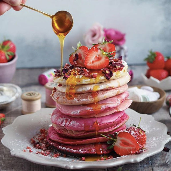 Pink Ombre Pancakes with syrup drizzling and fruit on top. 