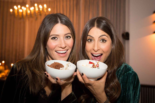 Two females smiling holding white bowls of food.  