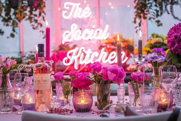 Mixed pink table setting with flowers, candles and The Social Kitchen in pink text lighting. 