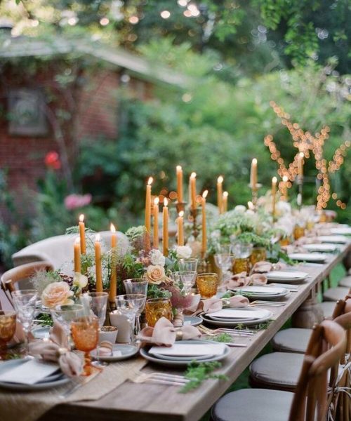 Outdoor table setting on long wooded table, flowers, candle and greenery. 