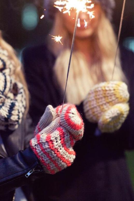 Two females wearing mittens holding sparklers. 