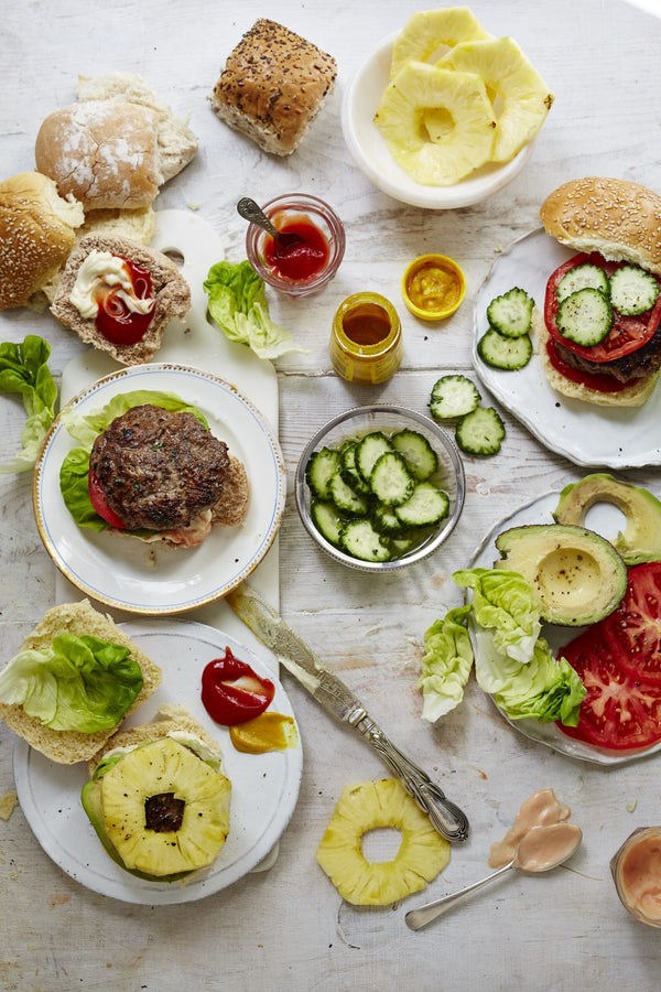 Top view of burgers and toppings on a white table. 