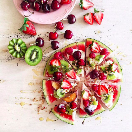 Top view of pie sliced watermelon topped with fruits on table. 