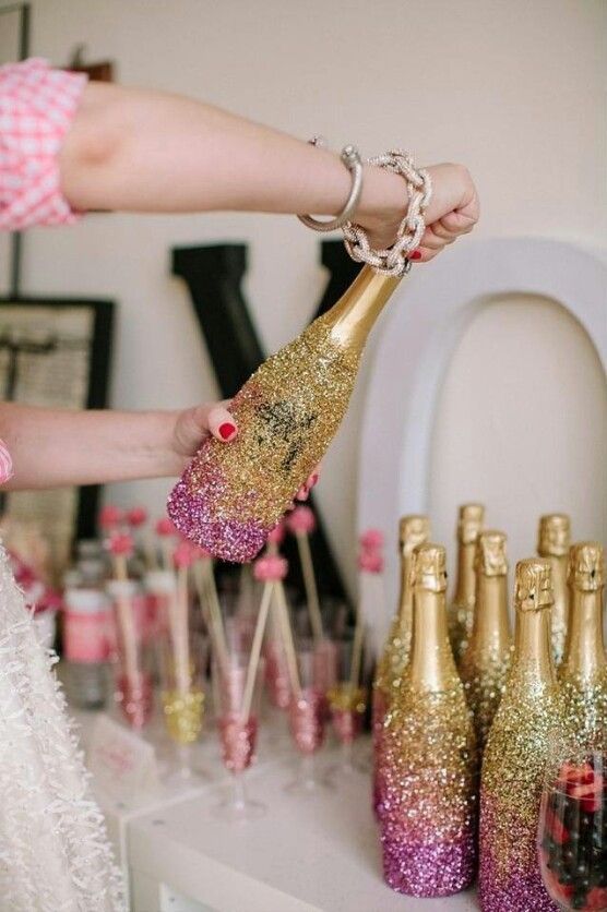 Female opening gold and pink sparkled champagne bottle with additional champagne bottles on table. 