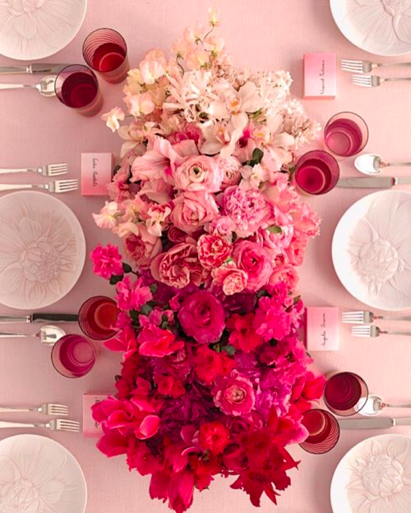 Top view of light pink to dark pink roses surrounded by table settings on a pink tablecloth. 