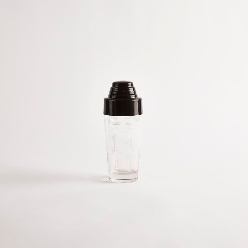 Vintage glass cocktail shaker with black plastic lid and measurement recipes designed on the side.