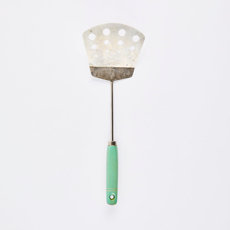 Silver slotted turner with green handle.