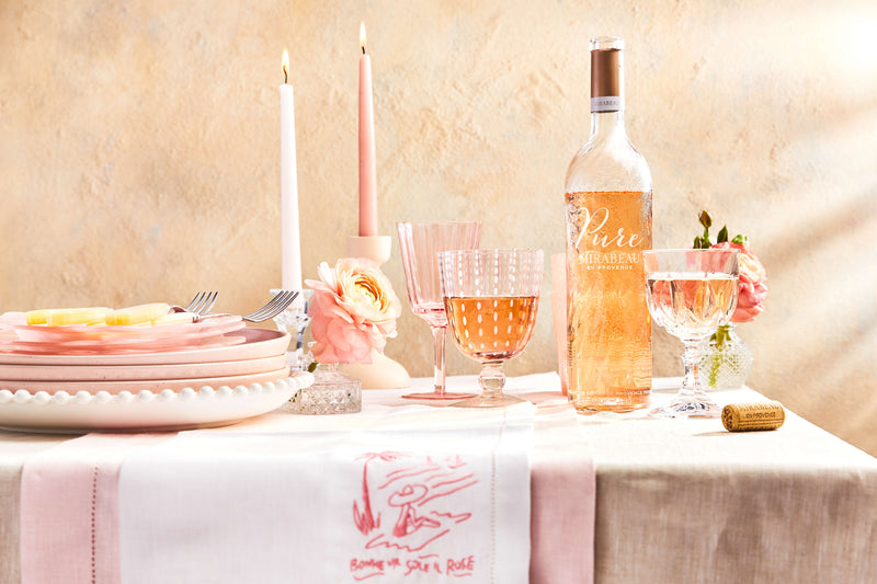 Side shot of Mirabeau x TSK edit with glassware, tableware and two bottles of Mirabeau against a sand background