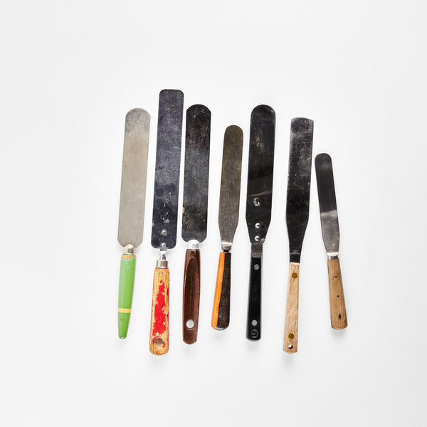 Seven silver pallete knives with wood multicoloured handles.
