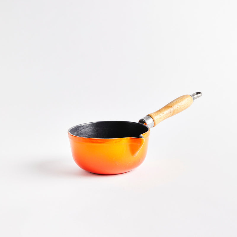 Orange ceramic pan with wooden handle.