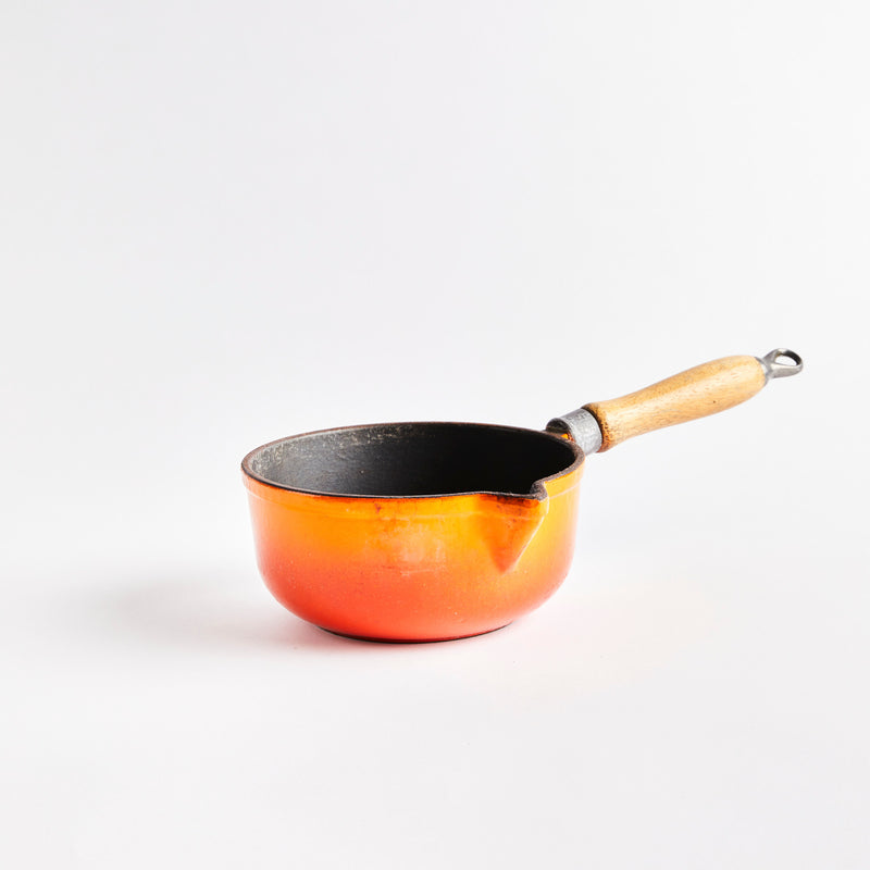 Orange ceramic pan with wooden handle.