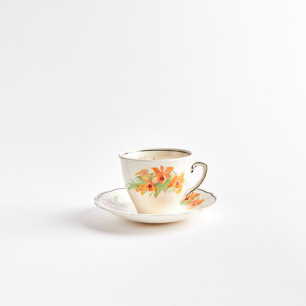 White teacup and saucer with orange and purple flowers.