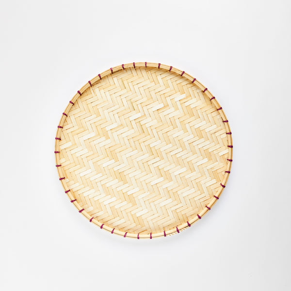 Round woven bamboo tray with purple stitching.