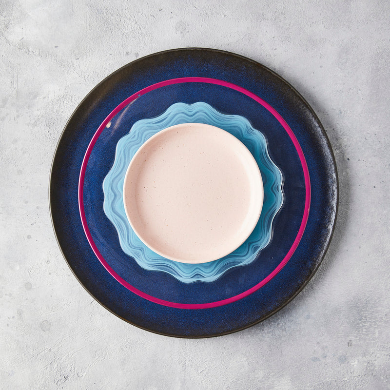 Top view of blue, pink and cream mixed plate settings with concrete background.