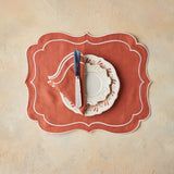 Top view of table setting with dark orange napkin and placemat on beige background.