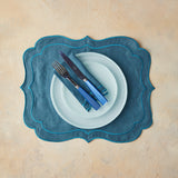 Top view of mixed blue table setting, cutlery, napkin and placemat on beige background.