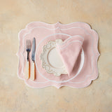 Top view of table setting with light pink napkin and placemat on beige background.