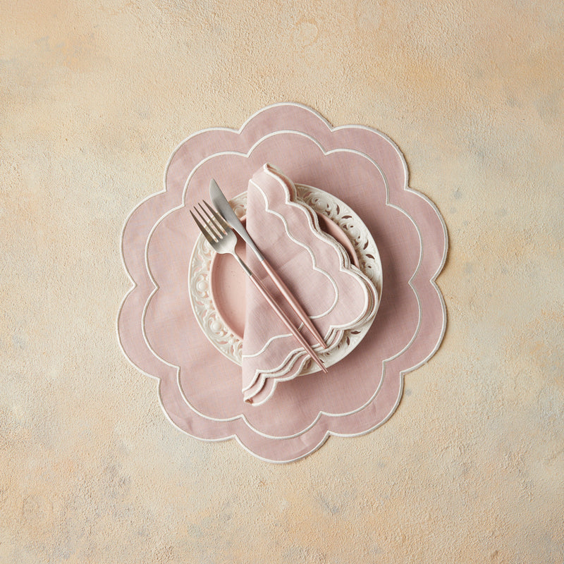 Top view of blush napkin and cutlery on white plate and blush scallop placemat with beige background.