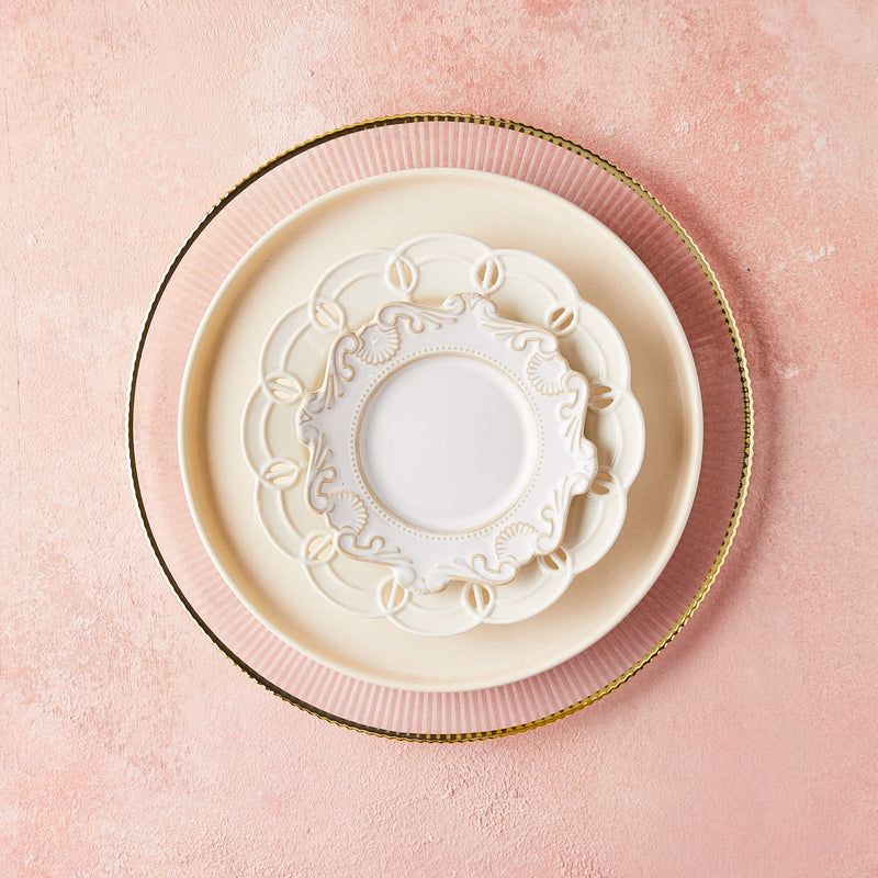 Top view of gold rim and cream mixed plates on pink background.