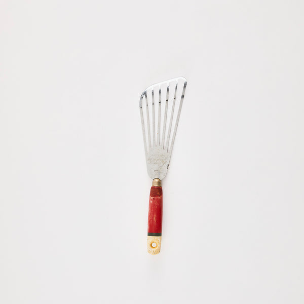 Silver slotted kitchen turner with red handle.