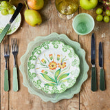 Top view of mixed green and floral detail table setting surrounded by variety of fruit on wooden table.