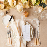 Top view of table setting surrounded by flowers and candles on beige tablecloth.