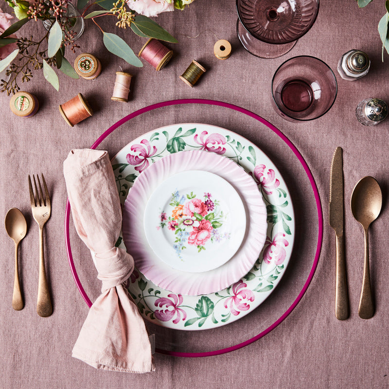 Top view of mixed pink table setting with gold cutlery surrounded by glassware on a pink tablecloth.