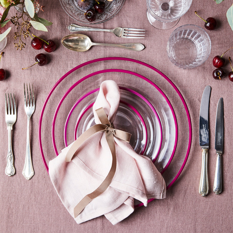 Top view of mixed pink table setting with gold cutlery surrounded by glassware on a pink tablecloth.