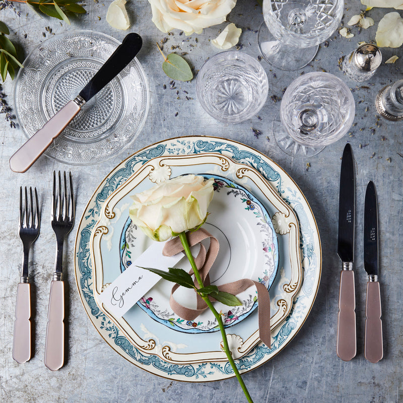 Top view of table setting surrounded by clear stemware and flowers on a concrete background.