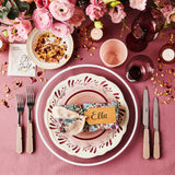 Top view of pink table setting surrounded by flowers and candles on pink tablecloth.