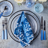Top view of black halo glass table setting with blue napkin, silverware and glassware on concrete background.